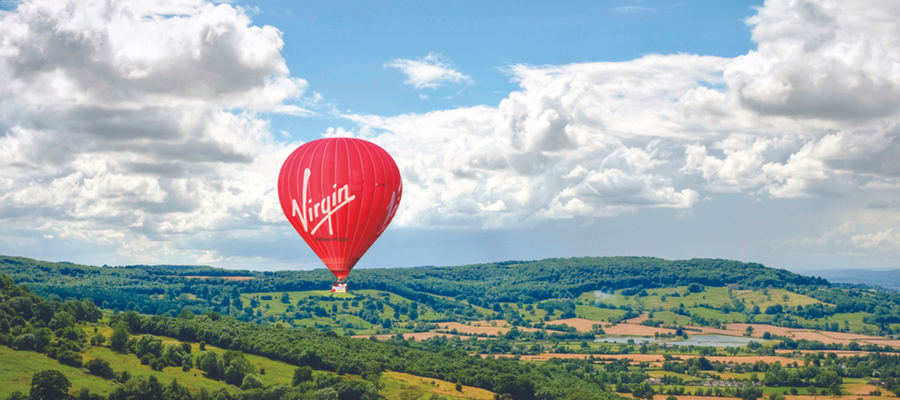 red virgin hot air balloon floating over countryside