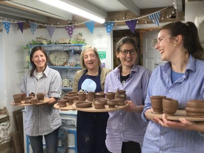 four ladies in a pottery workshop holding boards with their clay creations made during a pottery course experience day.