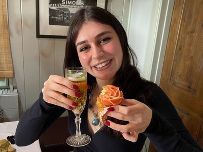 woman enjoying a champagne afternoon tea, holding a glass of champagne and a cupcake