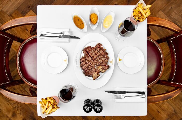 a view from above of a restaurant table laid out with a plate of steak in the middle, fries and sauces on the side