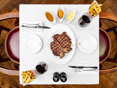 a view from above of a restaurant table laid out with a plate of steak in the middle, fries and sauces on the side