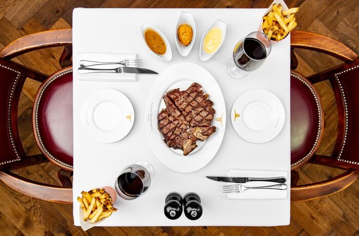 a view from above of a restaurant table laid out with a plate of steak in the middle, fries and sauces on the side