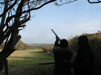 a person aiming a gun into the sky looked on by an instructor taking part in a clay pigeon shooting experience