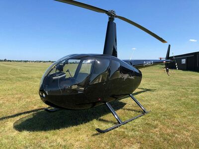 a black helicopter on grass against a blue sky as part of a helicopter flying lesson
