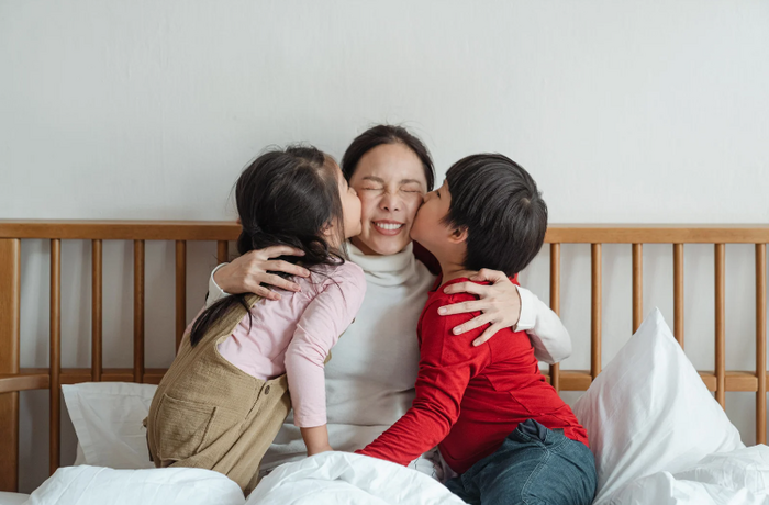 two children kissing their mum on the cheek sitting in bed to illustrate ideas for mothers day gifts