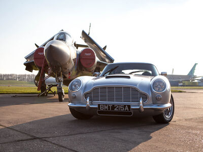 a british classic car next to an airplane on an airfield track