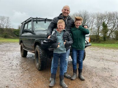 a man and two young boys standing in front of a 4 x 4 vehicle as part of a driving experience