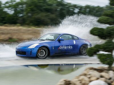 a blue sportscar driving through water on a track as part of a nissan and bmw drift battle experience day