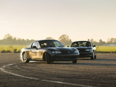 two black mx5 sports cars on a race track as part of a drifting experience