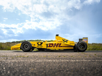 a side view of a yellow jordan formula one race car on a race track  against a cloudy sky background