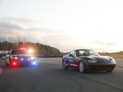 a police car with flashing lights chasing a black sports car on a race track as part of a police pursuit experience