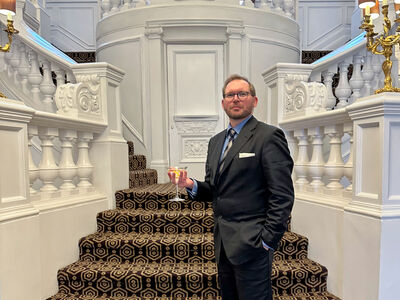 man wearing smart suit holding a martini in front of a grand staircase as part of james bond tour