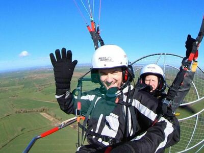 man smiling and waving while in the air on a paramotoring experience