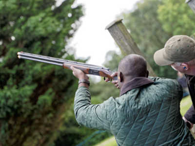 man pointing shotgun to the sky with instructor looking on as part of clay pigeon shooting experience