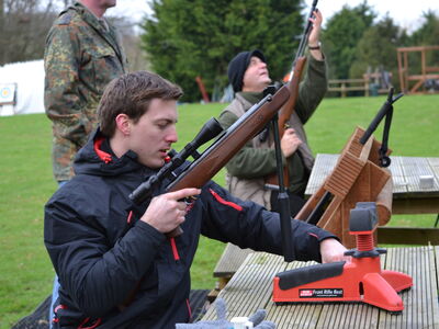 man sitting at table outside holding an air rifle as part of an air rifle shooting experience with instructor in background